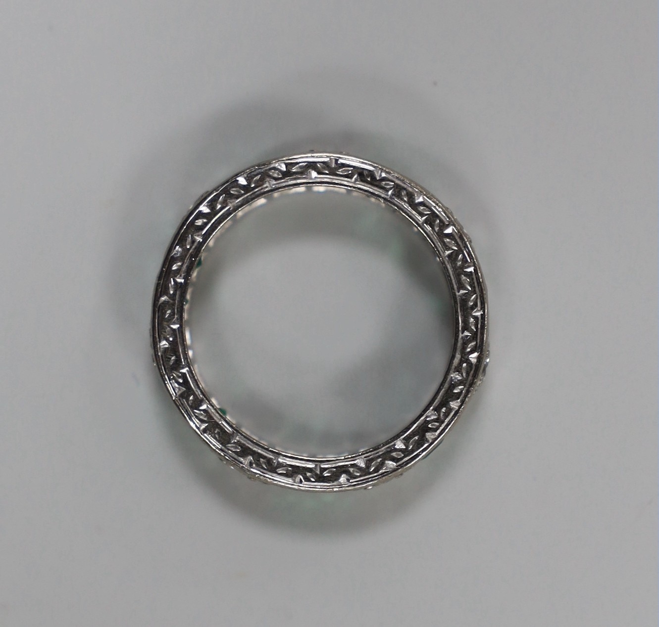 A mid 20th century 18ct white metal, emerald and diamond set full eternity ring (a.f.), size M/N, gross weight4.9 grams.